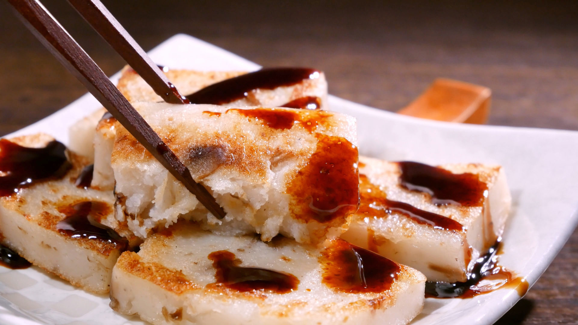 Pouring black soy sauce on ready-to-eat delicious turnip cake, Chinese traditional local dish radish cake in restaurant.