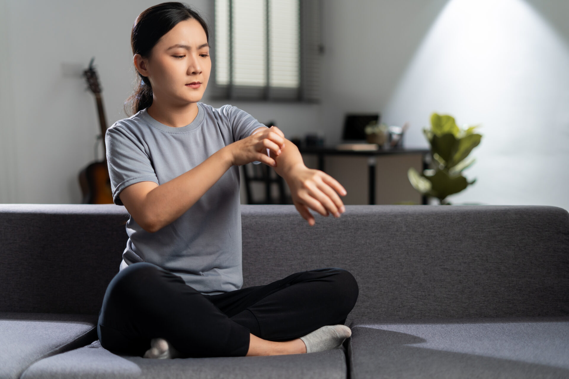 Asian woman was sick with irritate itching her skin sitting on sofa at home.